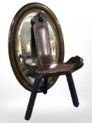 A carved stool on three legs, together with an oval Edwardian bevelled mirror.