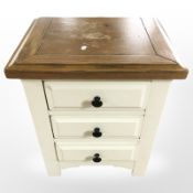 A cream three drawer chest with oak top,