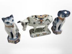 A Delft cow and a blue and white figure of a seated cat and dog signed 'Makkum', tallest 18 cm.