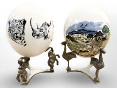 A pair of hand decorated ostrich eggs on Far Eastern brass stands,