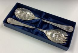 A cased pair of silver servers with berry decoration.