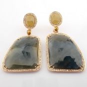 Gold earrings detailed with slice cut rough sapphire in the centre and brilliant diamonds on frame..