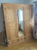 A pine wardrobe comprising of central mirrored door flanked by two panel doors with three drawers