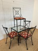A black wrought iron glass topped breakfast table and four accompanying chairs with red ground