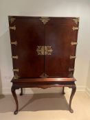 A cocktail cabinet on stand with brass banding to doors opening to reveal sliding drinks stands (