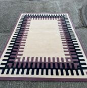 A beige ground rug with a black and mauve geometric boarder 290cm x 220cm