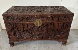 A Chinese ornately carved camphor wood chest with brass fittings and featuring a desert scape