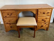 A pine kneehole dressing table flanked by six drawers on either side with cream upholstered stool (