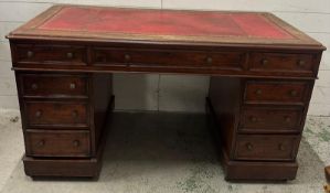 A red leather topped pedestal desk with a central long drawer flanked by four drawers on either side