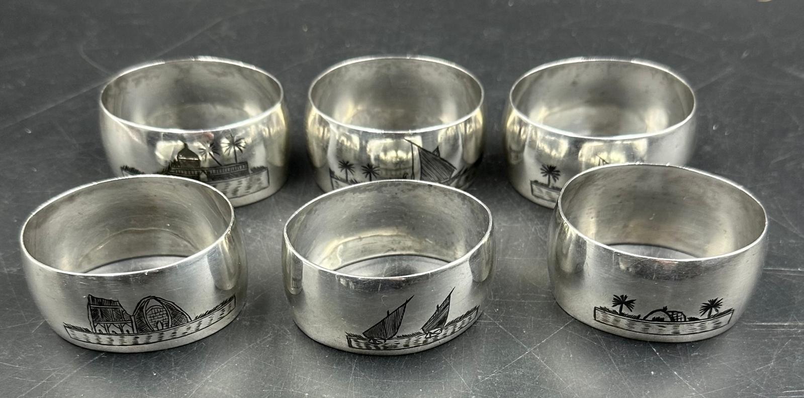 A set of six white metal Persian napkin rings with various scenes displayed on them.