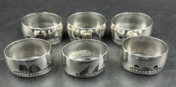 A set of six white metal Persian napkin rings with various scenes displayed on them.