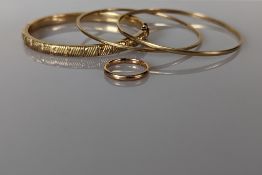 A gold hinged bangle with textured design, some dents/holes; two plain gold bangles