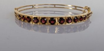 A 9ct yellow gold hinged bangle of tapering form with eleven graduated garnets, largest 0.50 carats
