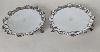 Two George III silver card trays with ornate pie-crust border and scroll motifs, raised on four hoof