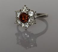 A diamond cluster ring with a central orange/brown 'cognac' natural diamond in a claw setting 