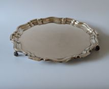 A George VI circular silver tray with pie-crust border on three scroll feet, hallmarked 