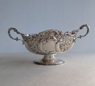 A late Victorian silver twin-handled oval basket with embossed decoration on a raised foot