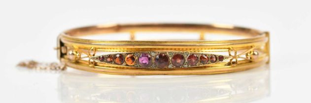 A 9ct yellow gold hinged snap bangle, set with ten garnet coloured stones and one amethyst