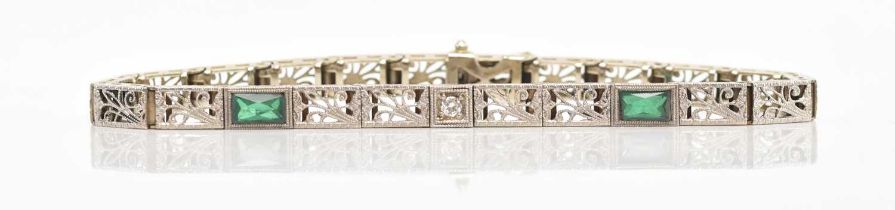 A white metal diamond and emerald set tennis bracelet, set with a central brilliant cut diamond