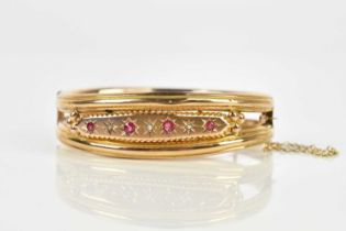 A Victorian yellow metal diamond and red stone set hinged bangle, unmarked, approx 11.1g, boxed.