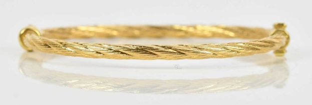 A textured yellow metal hinged snap bangle, stamped '750', approx 9.6g.