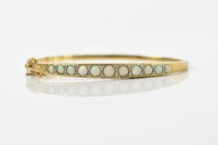 A yellow metal opal and diamond set hinged bangle, stamped 375, set with eleven opals and a melle of