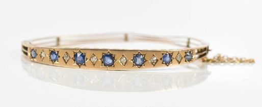 A Victorian yellow metal hinged bangle, stamped 9c, set with seven sapphires and six diamonds, width