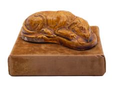 A press moulded pottery figure of a recumbent hound, under pale treacle glazes, 9.5cm long.