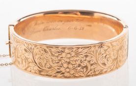 A 9ct gold bangle, with floral and foliate engraved decoration to front panel, hinged,