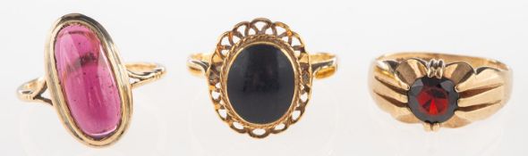 A group of three rings, including a ring set with an elongated oval cabochon red stone,