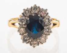 A sapphire and diamond cluster ring, claw set to the centre with an oval-cut dark blue sapphire,