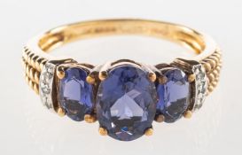 A 9ct gold purple stone and diamond ring, claw set with three oval-cut purple stones,