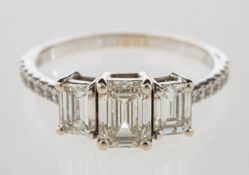 A three stone emerald-cut diamond ring, set to the centre with an emerald-cut diamond,