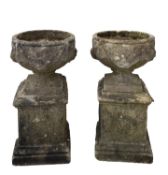 A pair of stone composition garden urns on plinths,