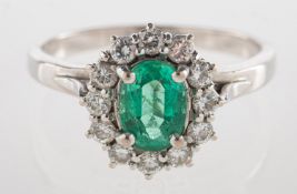 An emerald and diamond cluster ring, claw set to the centre with an oval-cut emerald,