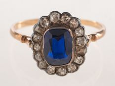 A cluster ring, collet set with an emerald-cut synthetic sapphire,