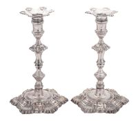 A pair of George II cast silver candlesticks, on shaped circular bases with shell decoration,