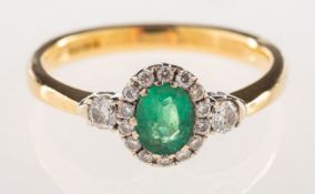 An 18ct gold emerald and diamond halo ring, claw set to the centre with an oval-cut emerald,
