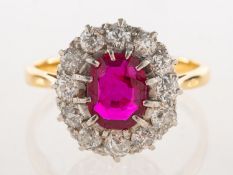 A ruby and diamond cluster ring, claw set to the centre with an oval-cut ruby,
