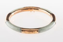 A hinged jade bangle, with foliate carving to yellow metal sections, push in clasp, safety chain,