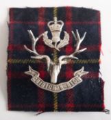 An Officer's Silver Queen's own Highlanders bonnet badge. Mounted on a piece of tartan.