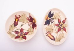 Two pieces of Walter Moorcroft pottery tube lined in the Columbine pattern reserved on an ivory