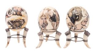 A set of three painted Ostrich eggs on stands, 20th century; decorated respectively with elephant,