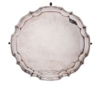 A George V silver salver, of shaped circular outline, with a moulded border and on four hoof feet,