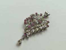 A white gold diamond and ruby set pendant, the flo