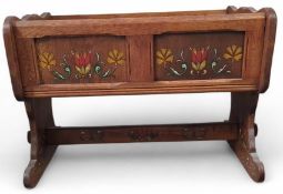 An oak rocking cot with painted floral features in