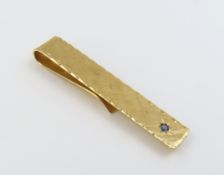 A gold tie slide marked ‘14K’ set with a sapphire