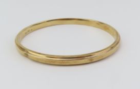 A gold bangle, marked '9ct' with fine engrave