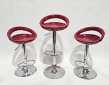 Three retro style modern red and chrome adjustable bar stools, each with footrest and circular