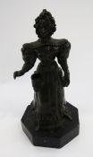 Bronze figure of a lady dressed in a bonnet and dress with aperture to her pocket, on octagonal